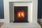 A Wave 5 insert cassette stove installed in a white marble fireplace and lighting